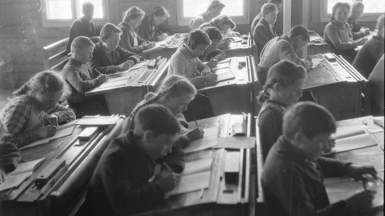 Blick in das Klassenzimmer der Schule Kien um 1942; die Kinder sitzen an Pulten und schreiben in Hefte
