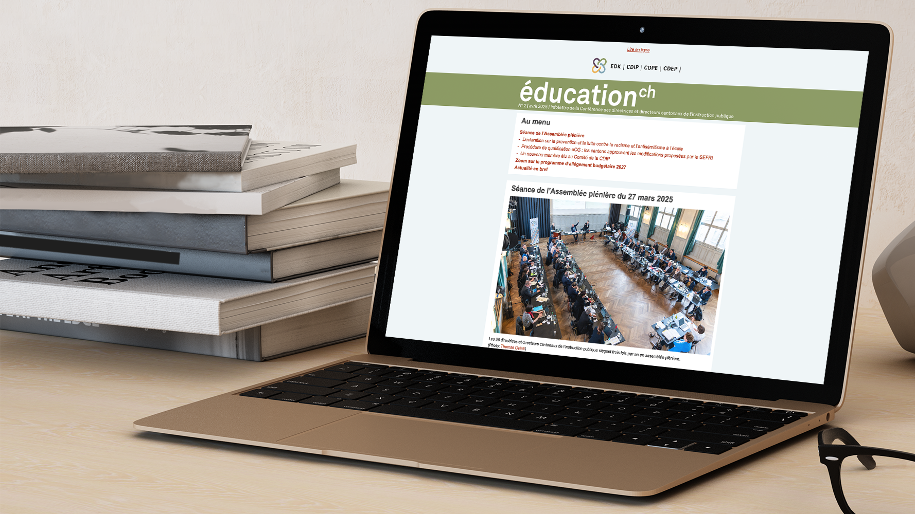 Laptop ouvert, montrant l’infolettre de la CDIP sur son écran; pile de livres posée à gauche du laptop