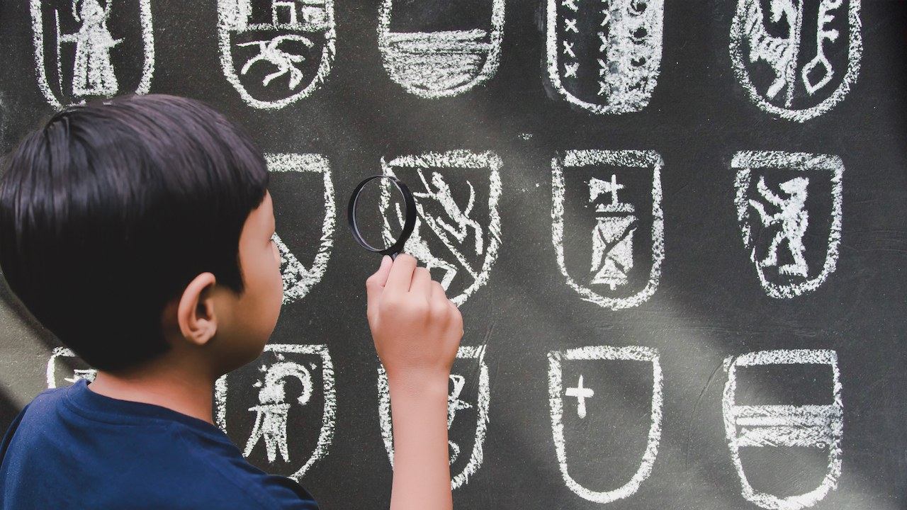 Un enfant observe à la loupe des écussons cantonaux dessinés sur un tableau noir.