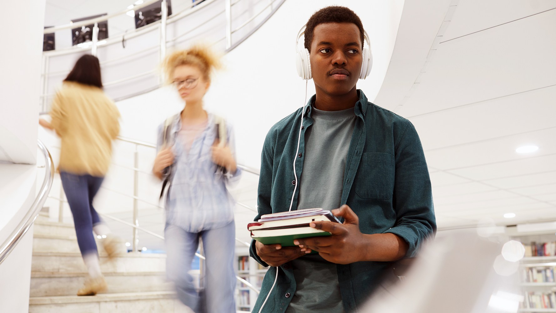 Un jeune étudiant descend un escalier dans une bibliothèque avec des livres dans les mains.