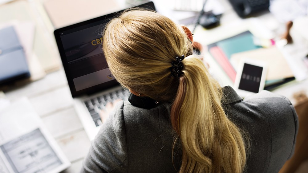Eine Frau arbeitet an einem Laptop, den Telefonhörer hat sie zwischen Schulter und Ohr geklemmt