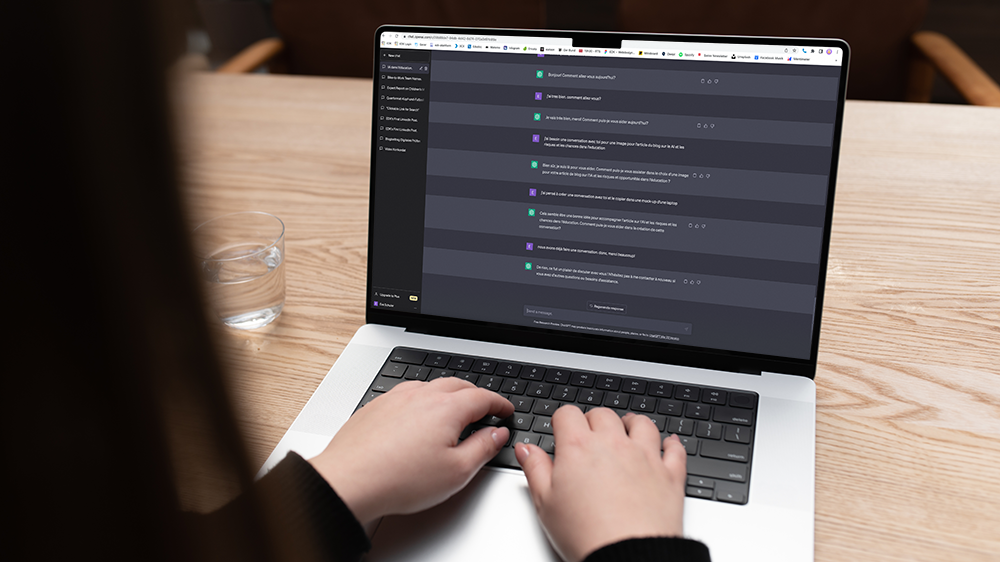 Vue par-dessus l'épaule d'une femme sur un ordinateur portable, sur lequel on peut voir un chat avec ChatGPT